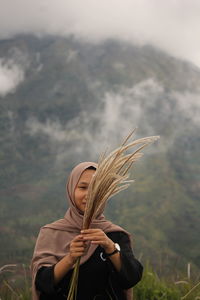 Woman holding plants while standing against mountain