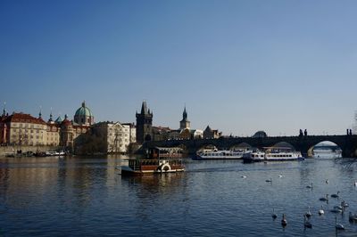 Bridge over river by buildings in city against clear sky