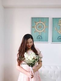 Beautiful woman holding bouquet while standing against wall