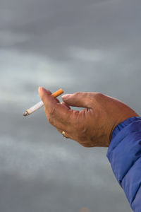 Close-up of hand holding cigarette against sky