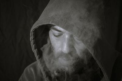 Man wearing hood clothing while smoking in darkroom