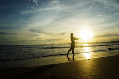 Silhouette woman standing on beach against sky during sunset