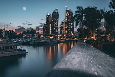 Illuminated buildings by river against sky at night