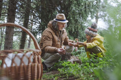 Grandfather and girl picking up mushrooms in forest