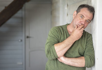 Portrait of serious mature man leaning on wall at home