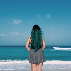 Rear view of woman with long hair standing at beach against blue sky