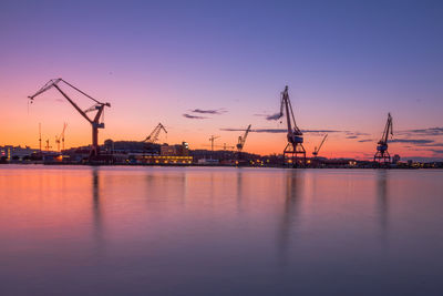 Cranes at commercial dock against sky during sunset