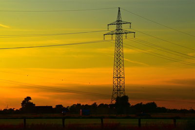 Low angle view of silhouette electricity pylon on field against romantic sky at sunset