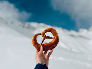 Cropped hand of woman holding pretzel against sky