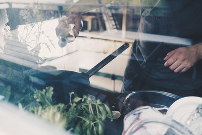 Midsection of man cooking food seen through glass window with reflection