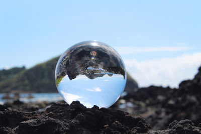 Close-up of crystal ball on rock against sky