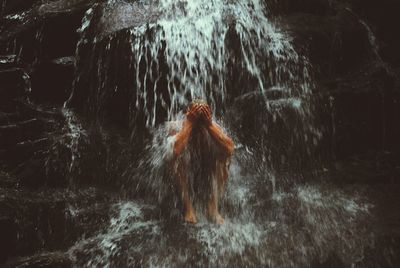 Full length of shirtless man sitting below waterfall