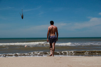 Rear view of shirtless man on beach against sky
