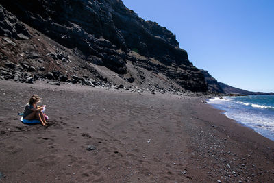 Man sitting on shore at beach against sky