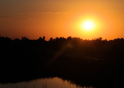 Silhouette trees by lake against sky during sunset