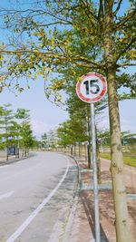 Road sign by trees against sky