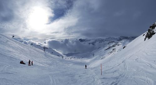 Panoramic view of people skiing on snowcapped mountain against sky