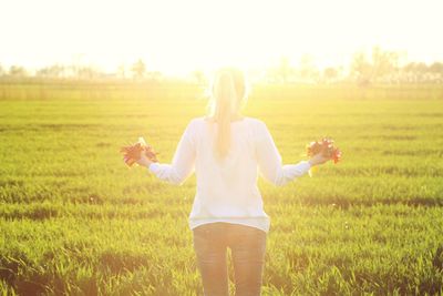 Rear view of woman holding flowers while standing on grassy field during sunny day