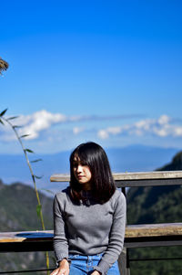 Young woman sitting at observation point against blue sky