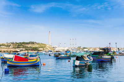 Boats moored at harbor against blue sky