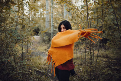 Woman wearing scarf standing against trees in forest