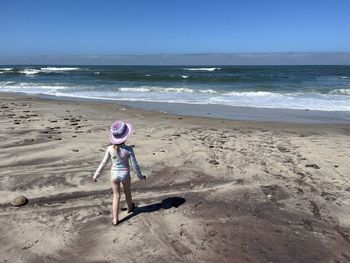 Rear view of woman standing at beach against sky