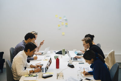 Multi-ethnic entrepreneurs sitting at conference table in illuminated board room during meeting