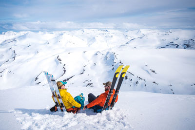 A man and a woman couple relaxing with skis with mountain backdrop