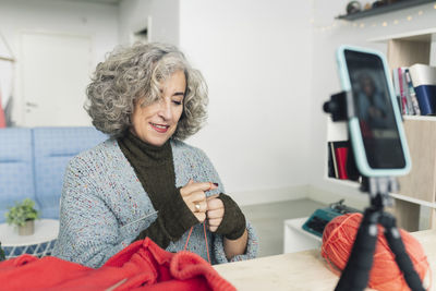 Senior vlogger making knitting tutorial through smart phone at home