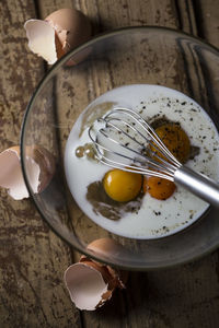 High angle view of wire whisk and eggs in bowl on table