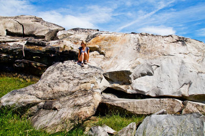 Female hiker sitting on rock formation against sky during sunny day