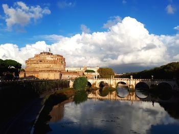 Arch bridge over river by buildings against sky