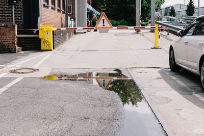 Caution sign on barrier over street with reflection in puddle
