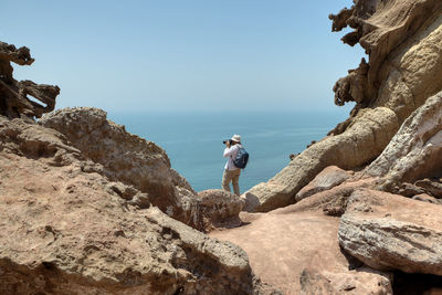 Man standing on rock by sea against sky