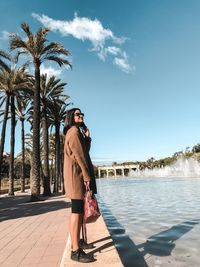 Woman standing by palm trees against sky