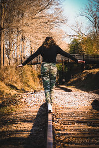 Rear view of woman standing on footbridge in forest