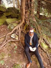 Portrait of young man sitting on tree trunk in forest