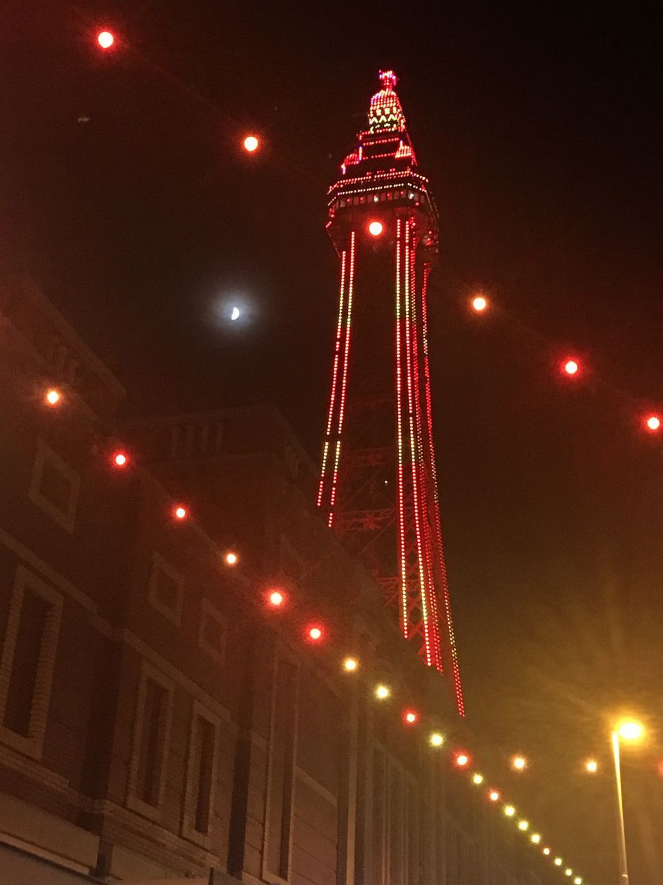 LOW ANGLE VIEW OF ILLUMINATED CHRISTMAS LIGHTS IN CITY AGAINST SKY AT NIGHT