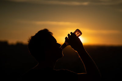 Silhouette man drinking beer against orange sky