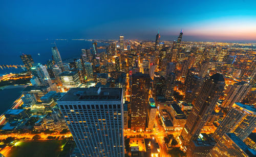 Aerial view of illuminated cityscape and sea at dusk