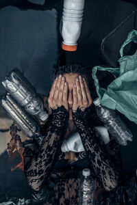 High angle view of woman covering face while lying on floor by bottles and plastic bag