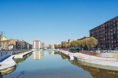 Reflection of buildings and trees in canal against clear blue sky