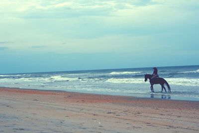 People riding horse at beach against sky