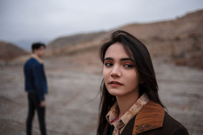 Portrait of young woman standing on desert against sky