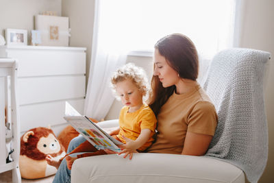 Mom reading book with baby boy toddler at home. early age children education development. 