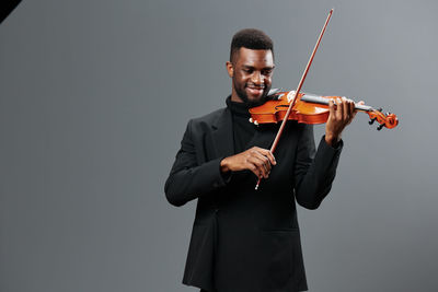 Young man playing violin against gray background