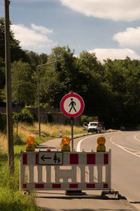 Road sign by trees against sky