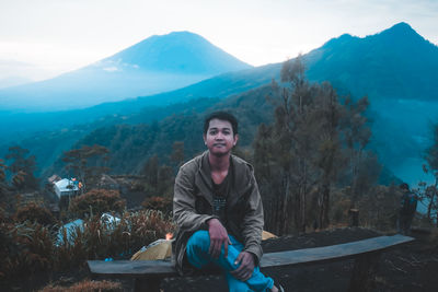 Portrait of young man sitting on mountain against sky