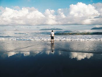 Rear view of man standing on beach against sky