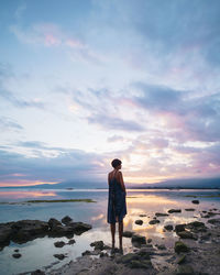 Rear view of woman standing on rock at beach